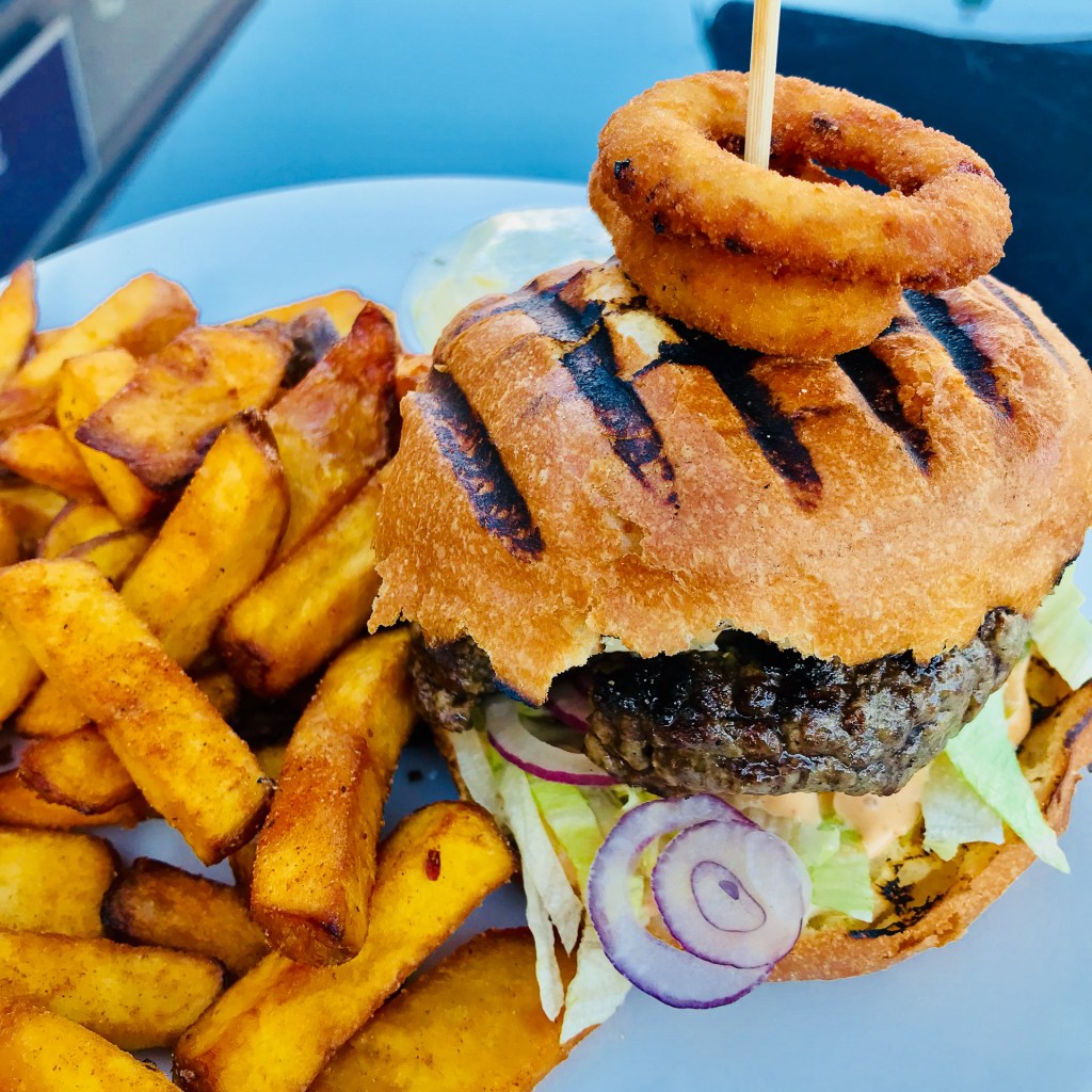 En hamburgare med en cirkel av lökringar på toppen och en portion pommes frites vid sidan.