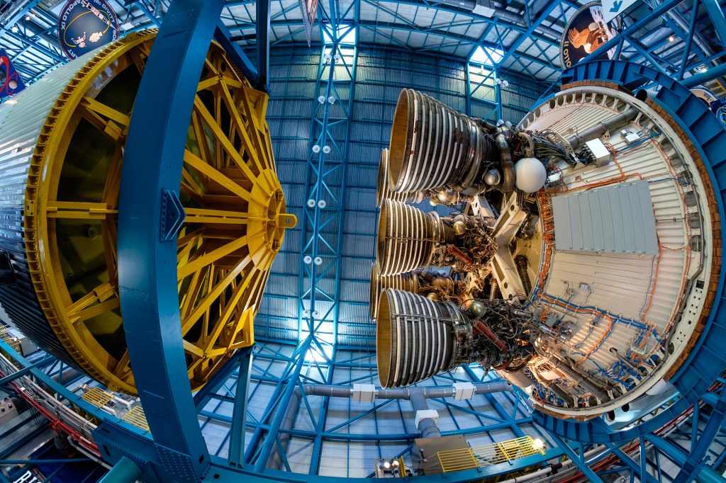 Detaljbild av en raketmotor som är utställd på Kennedy Space Center, med synliga komponenter och strukturer i en stor hall.