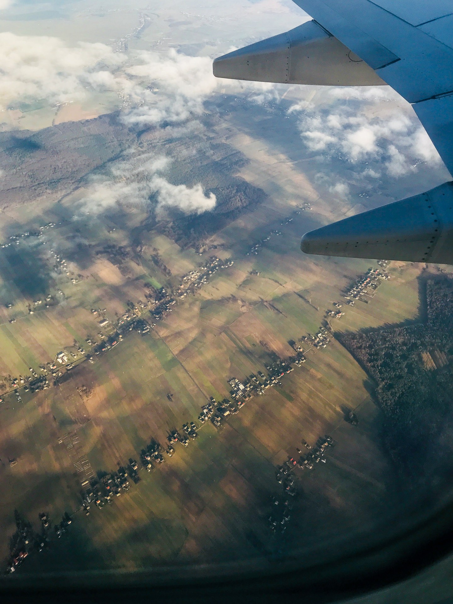 Utsikt från ett flygplansfönster över polska landskapet med fält, skog och moln.