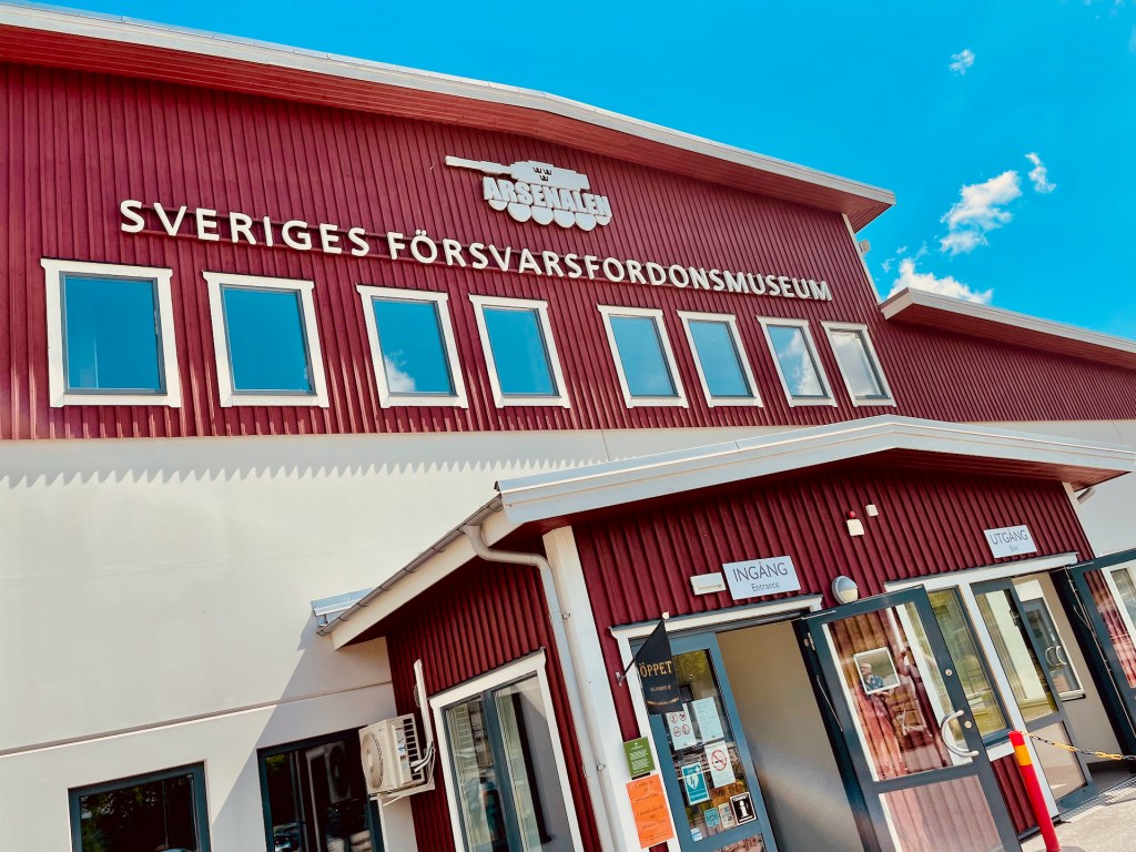 Entrén till Sveriges Försvarsfordonsmuseum med röd fasad och vita fönster.