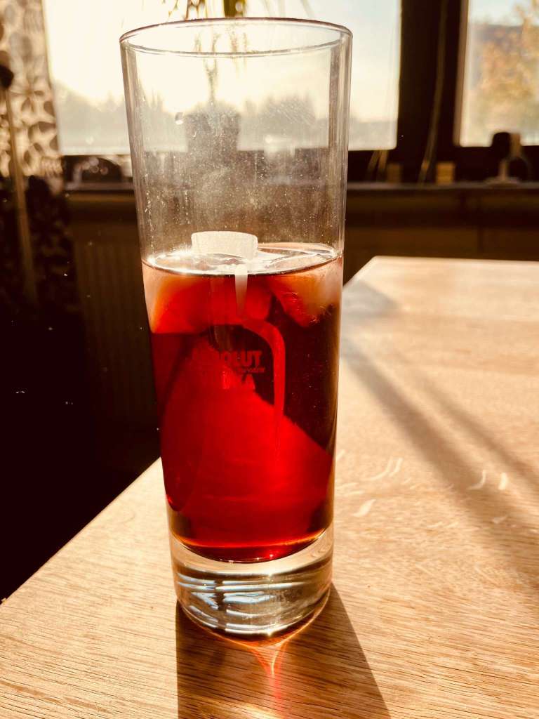 Ett glas med en röd drink, bestående av Dubonnet och gin, placerat på ett träbord i ett ljust rum.