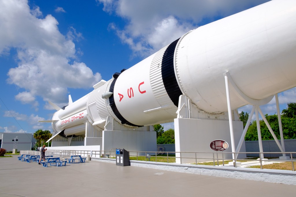 En stor raket visar en imponerande del av Kennedy Space Center, med en person i förgrunden som beundrar den.
