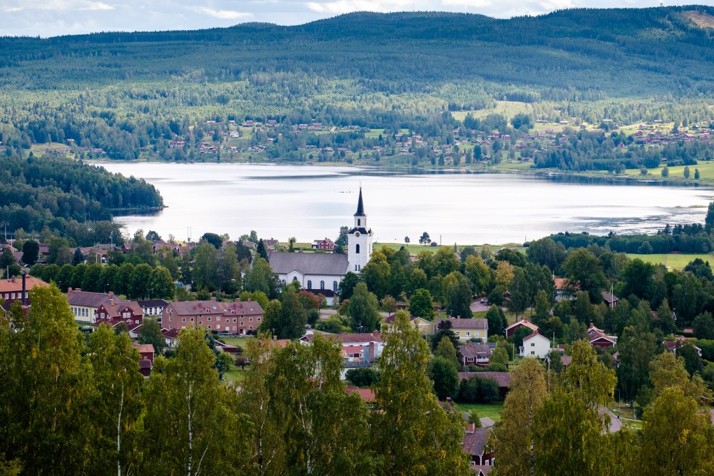 Utsikt över en svensk by med en kyrka och omgivande natur, med sjön Siljan i bakgrunden.