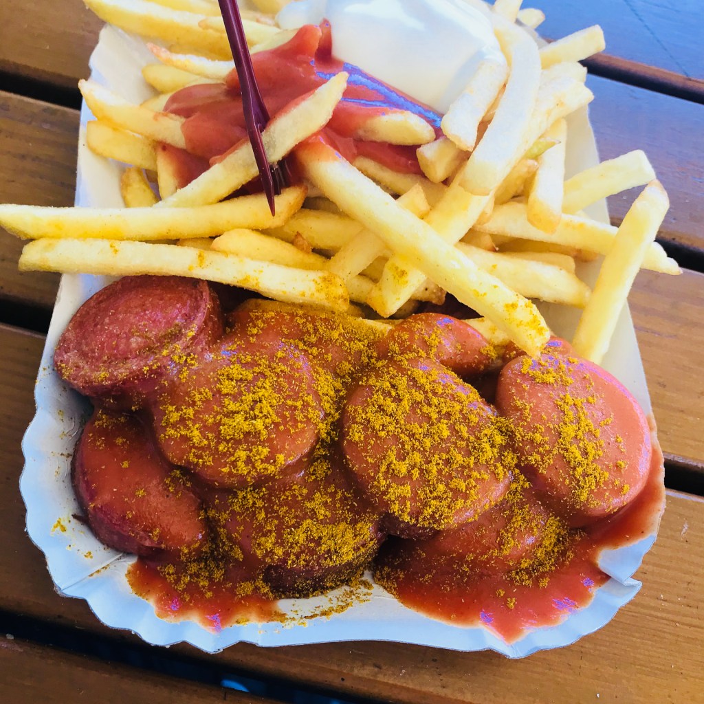 En tallrik med currywurst toppad med currypulver, serverad med pommes frites och ketchup.