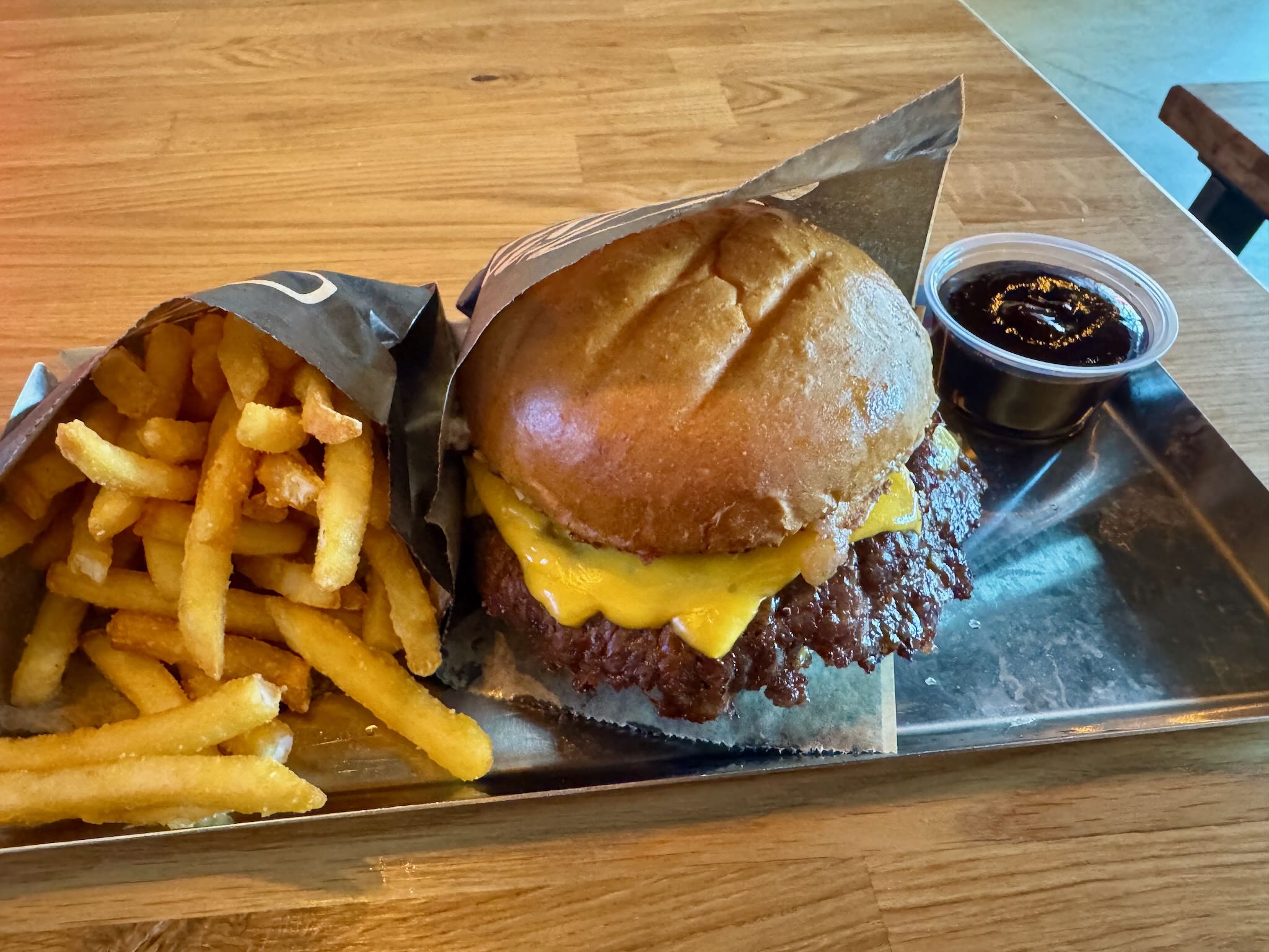 En saftig hamburger med smält ost, serverad med krispiga pommes frites och en liten skål med sås, på en metallfat.